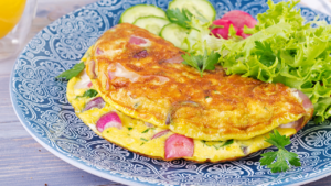 Omelett med diverse fyll på tallerken, grønn salat.